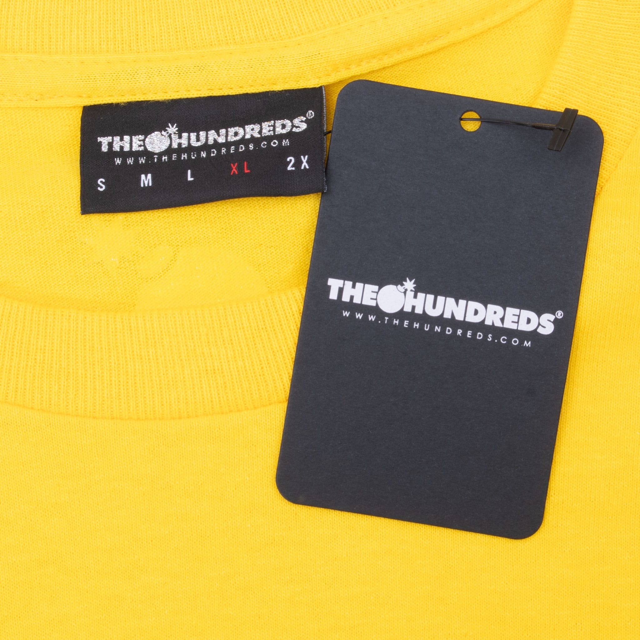 Close-up of The Hundreds XL neck label and attached black hangtag on yellow fabric