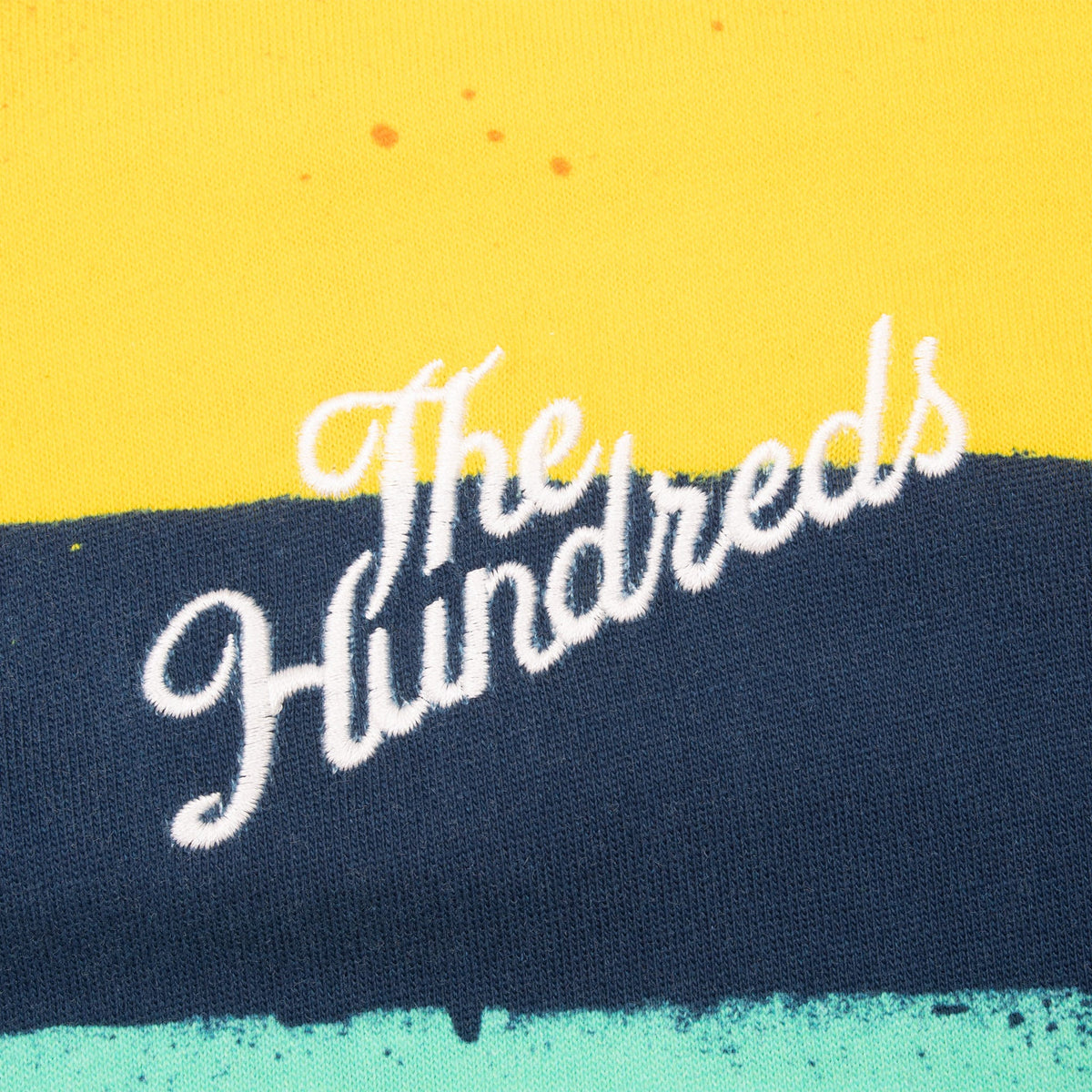 Close-up of white The Hundreds script embroidery on yellow and navy striped fabric