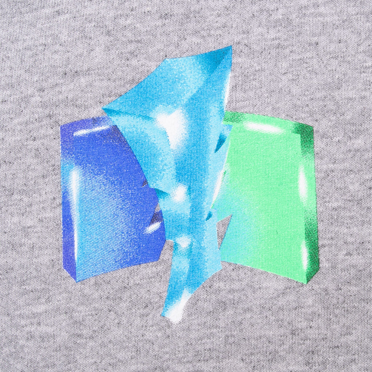 Close-up of small blue, aqua and green geometric left-chest print on grey T-shirt