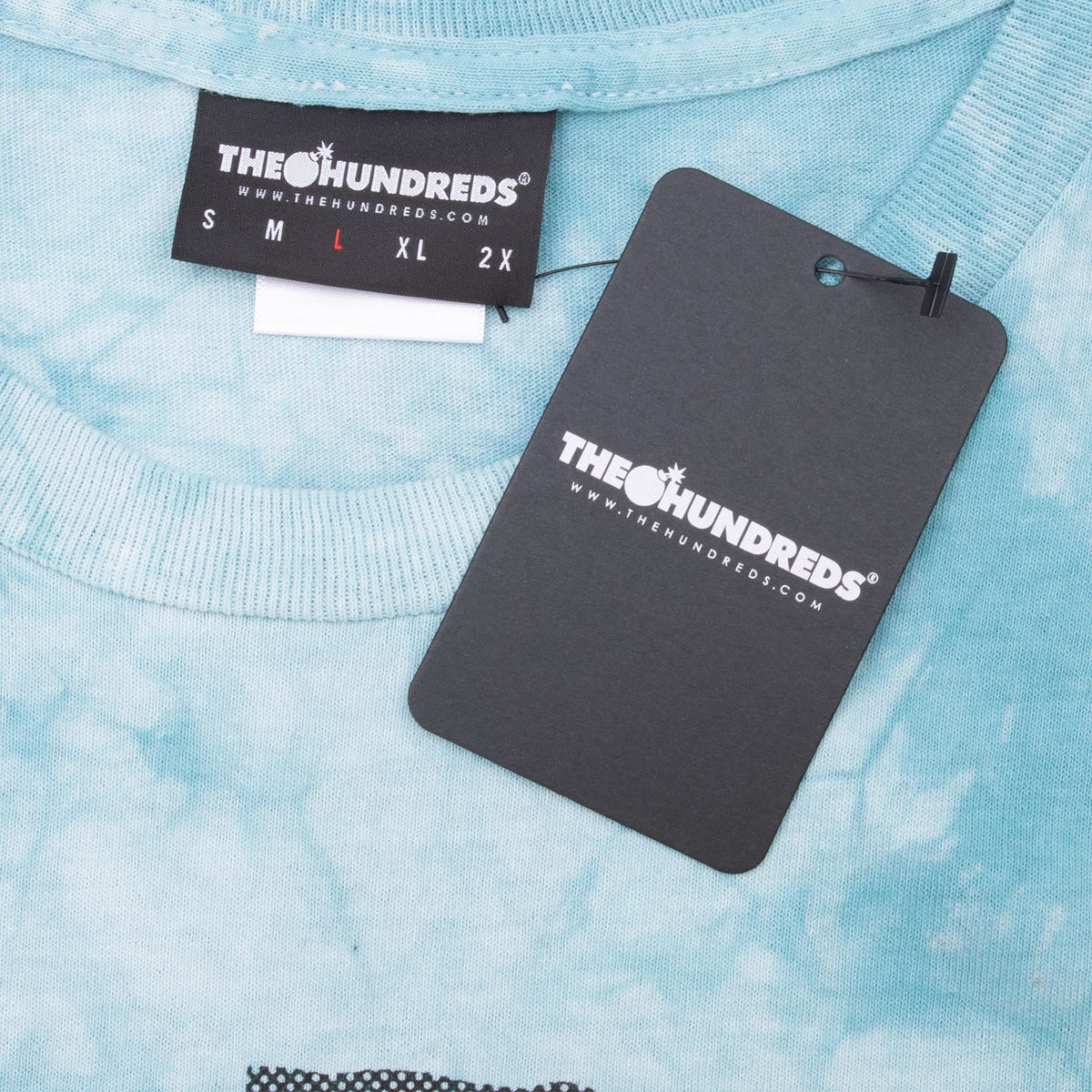 The Hundreds size large neck label and attached black hangtag on aqua tie-dye fabric