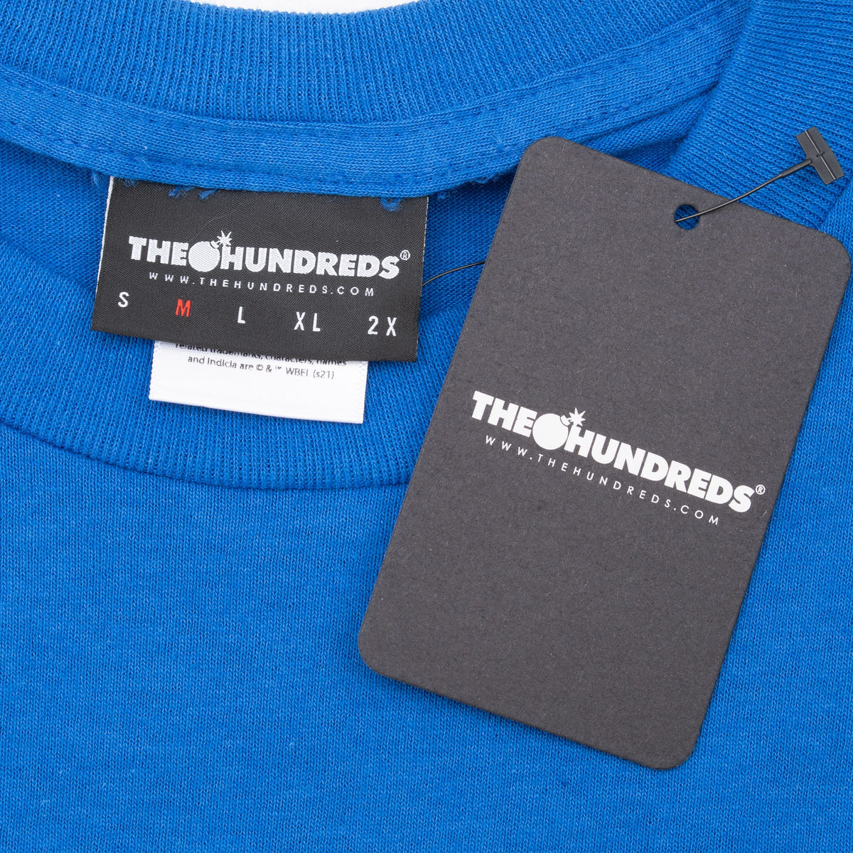 Close-up of The Hundreds neck label and attached black hangtag on blue T-shirt