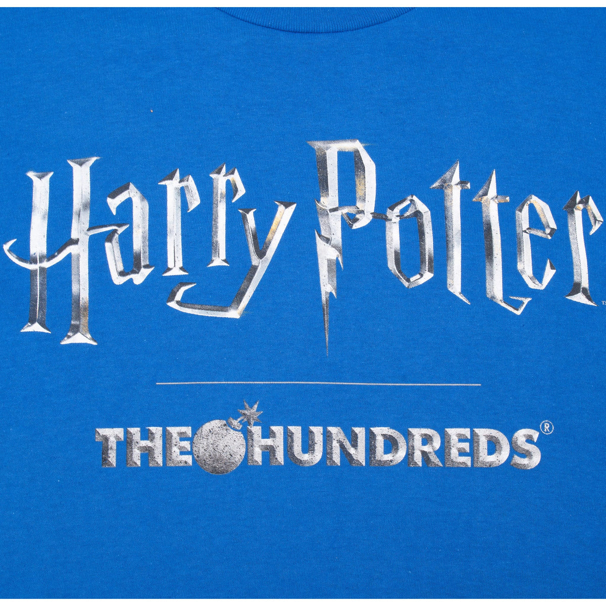 Close-up of silver-tone Harry Potter and The Hundreds chest graphic on blue T-shirt