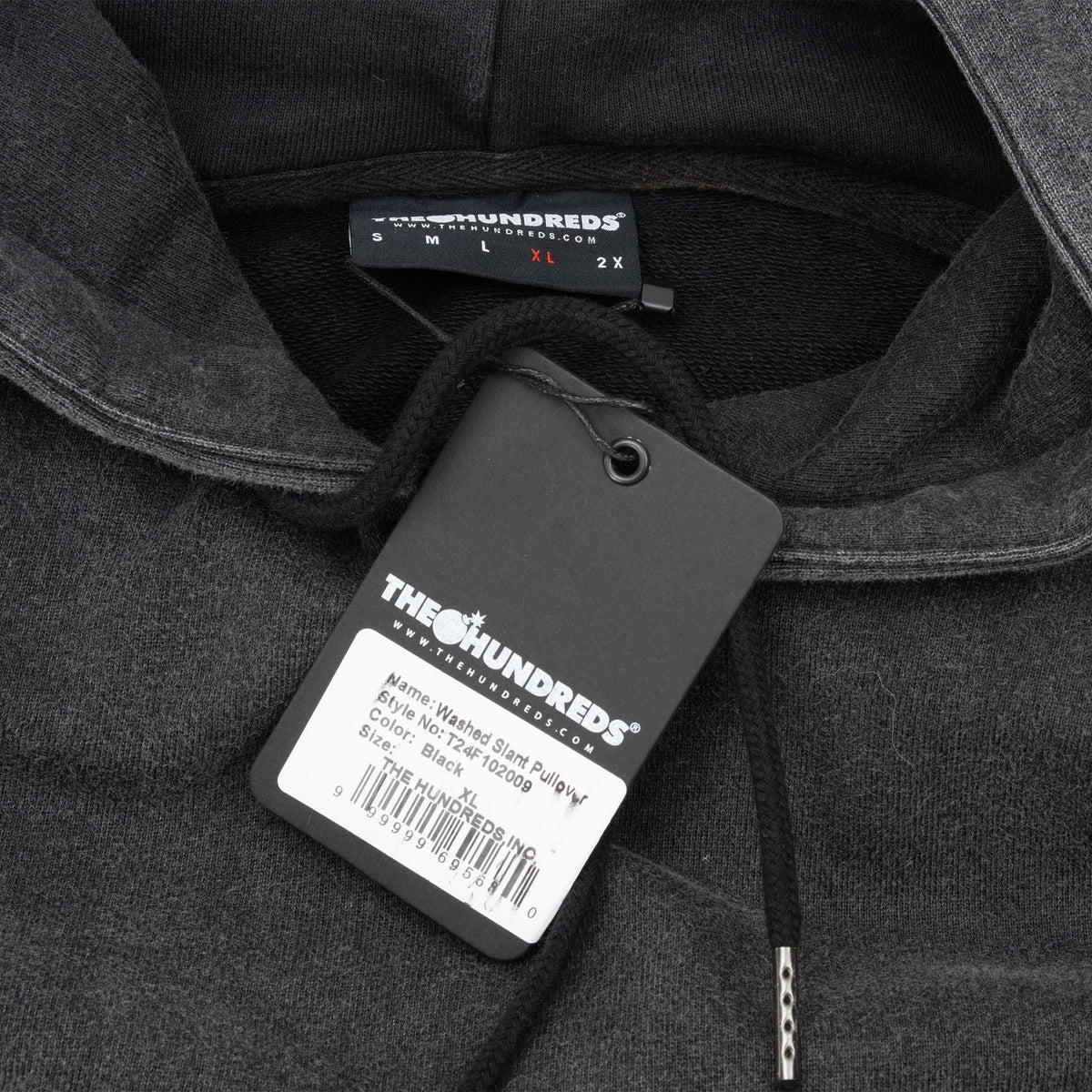 Close-up of The Hundreds neck label, attached hangtag, and metal-tipped hood cord
