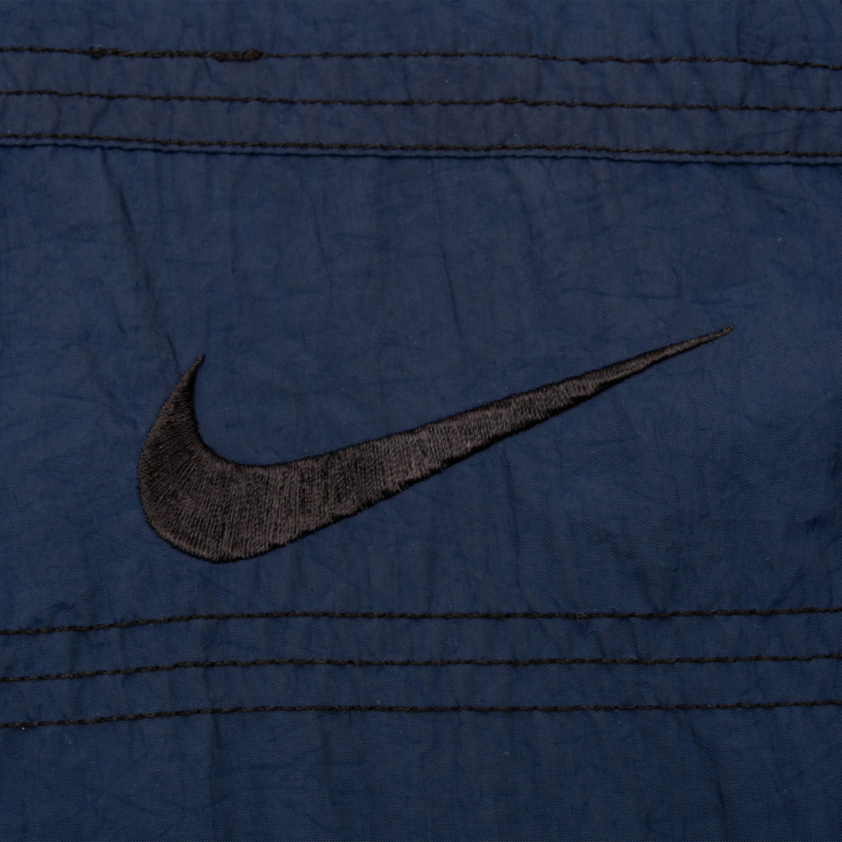 Close-up of black Nike Swoosh embroidery on blue windbreaker chest