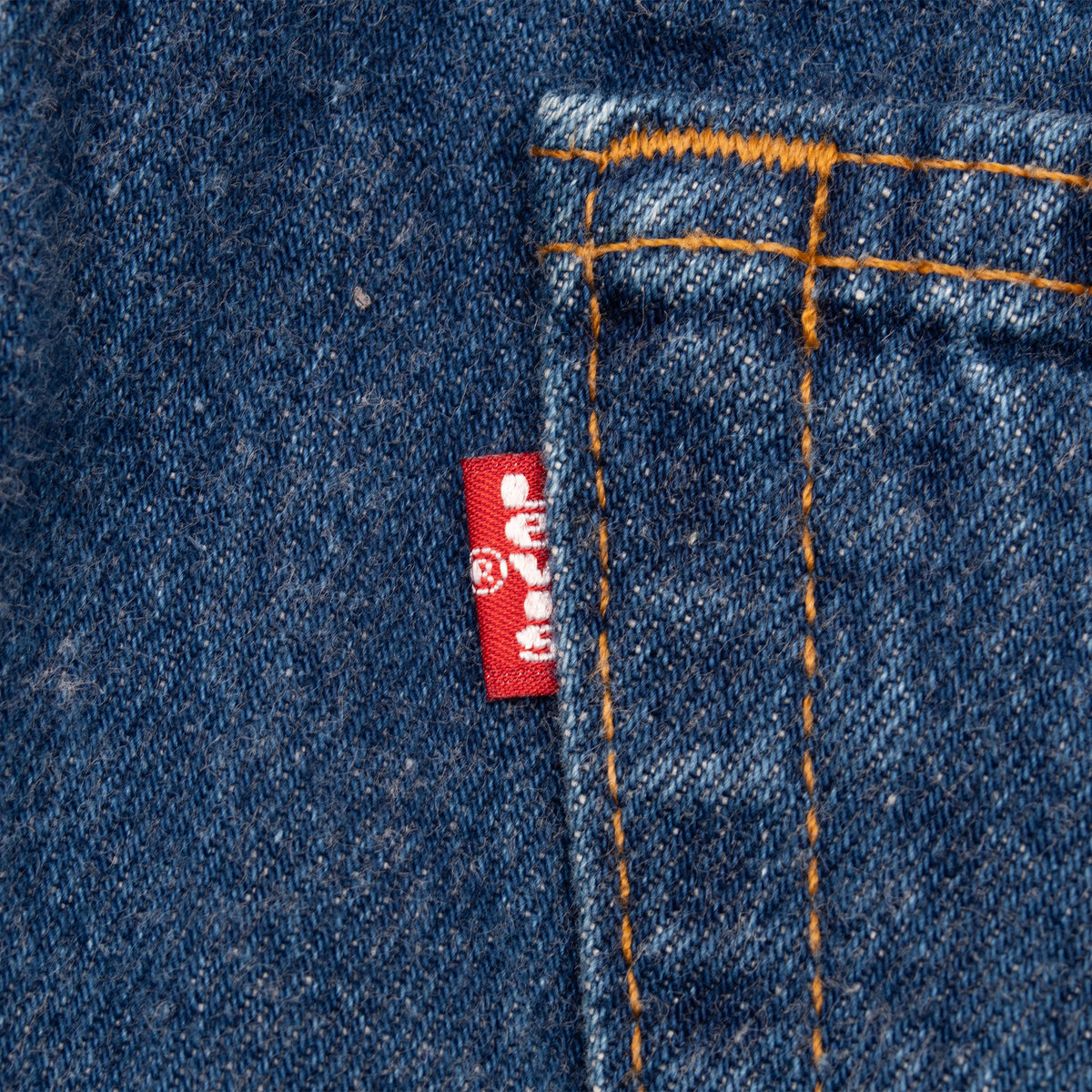 Close-up of red Levi's tab beside a back pocket seam on indigo denim