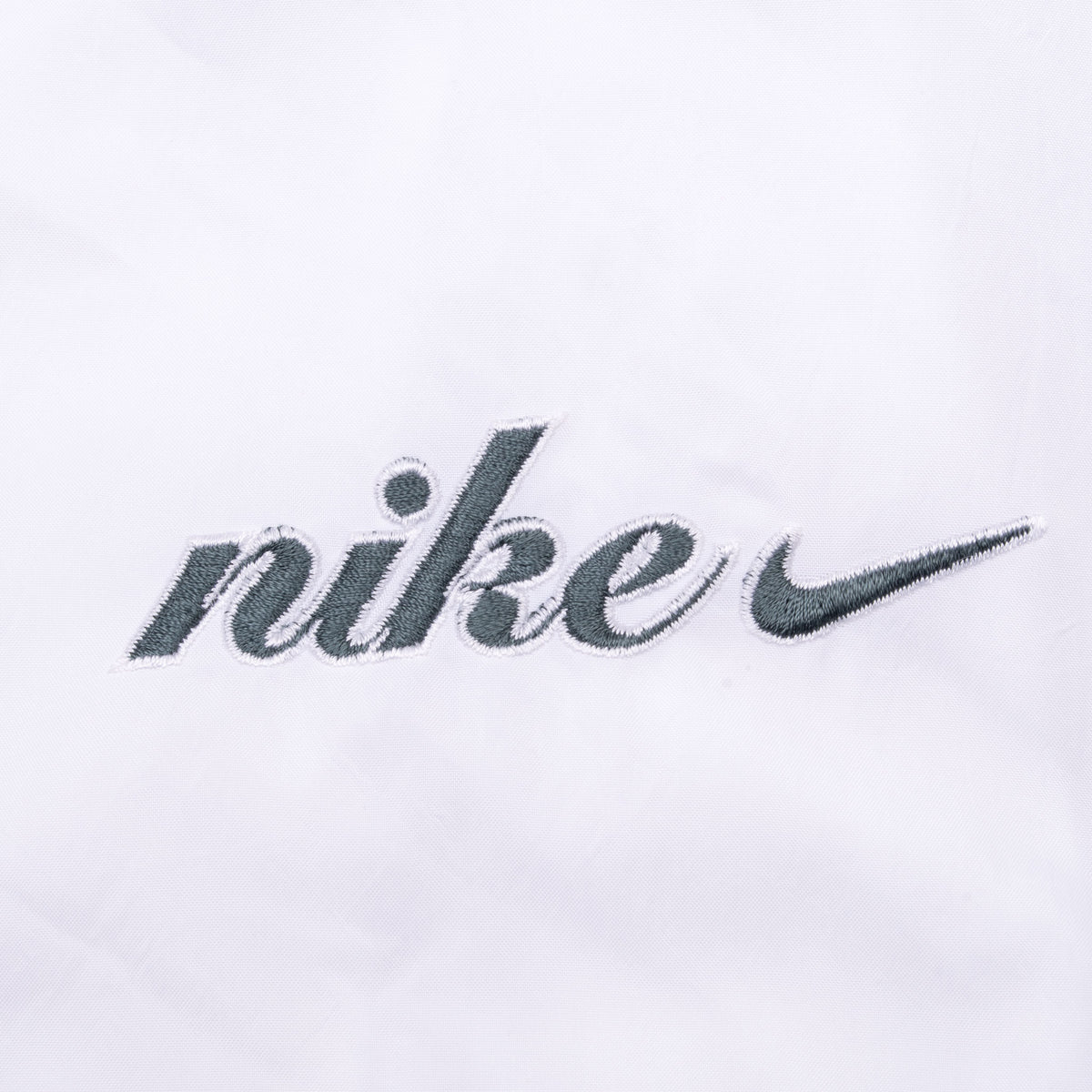 Close-up of gray Nike script and Swoosh embroidery on white fabric