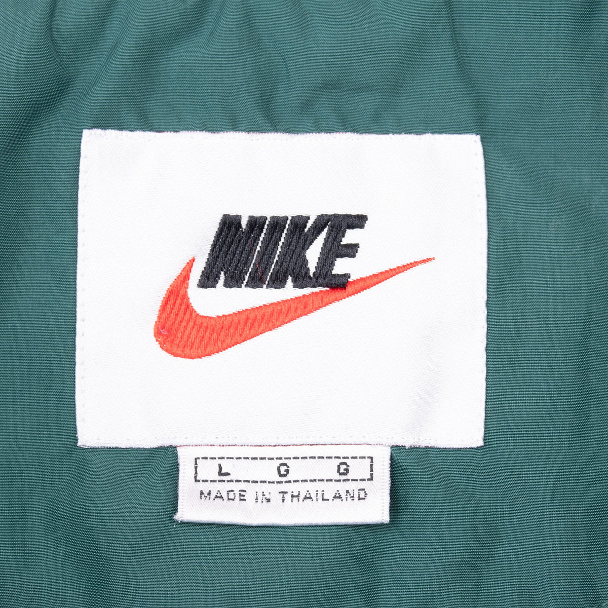 Nike neck label with black logo, orange Swoosh, and large size tag inside green jacket