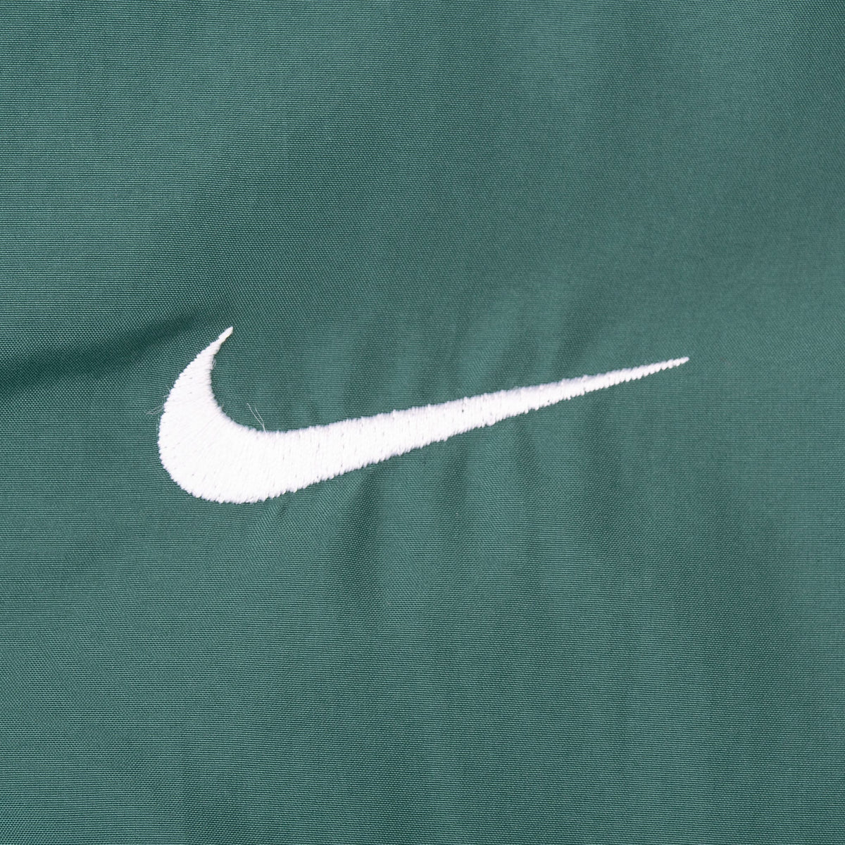 Close-up of white embroidered Nike Swoosh on green jacket chest