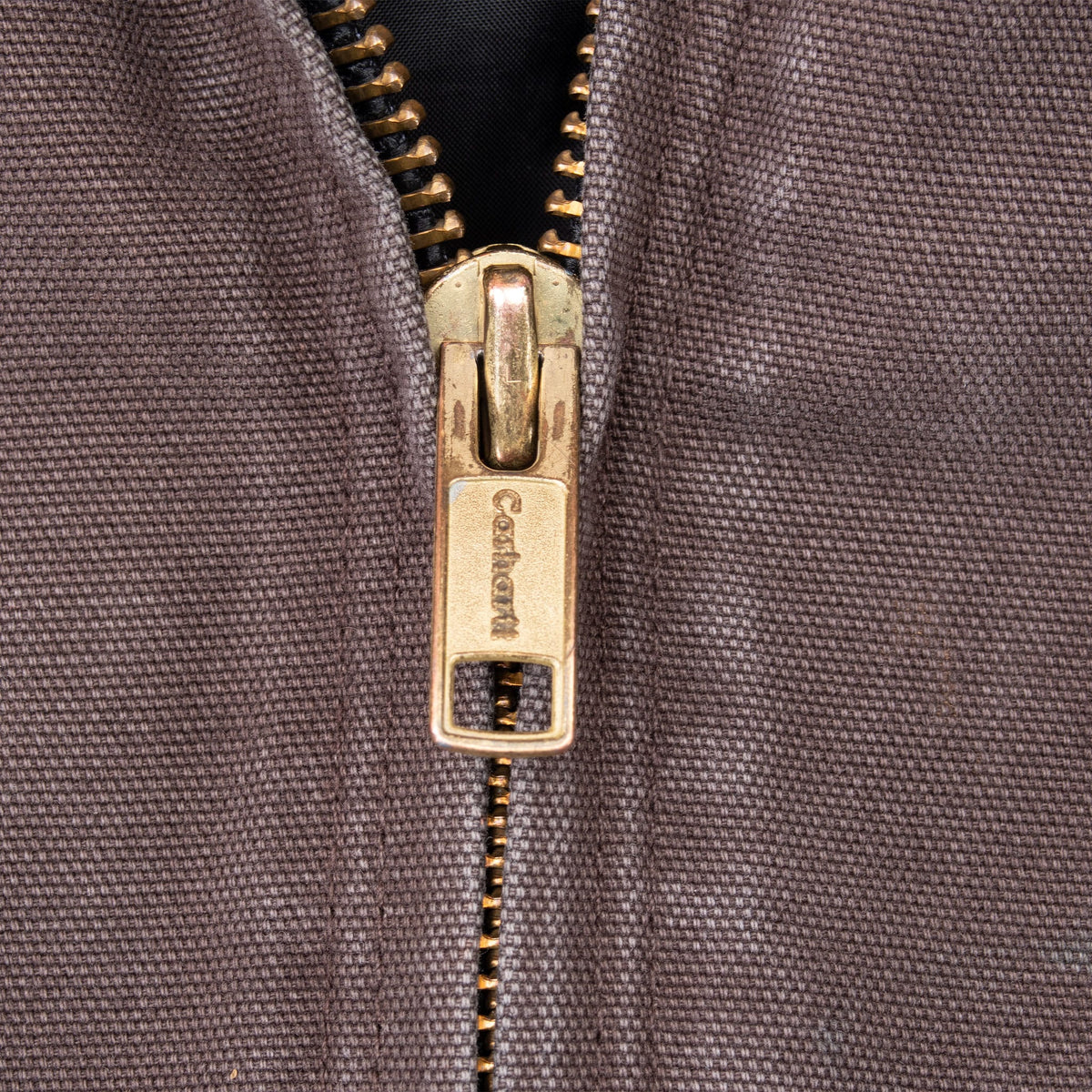 Close-up of brass-tone Carhartt-branded zipper pull on dark brown fabric