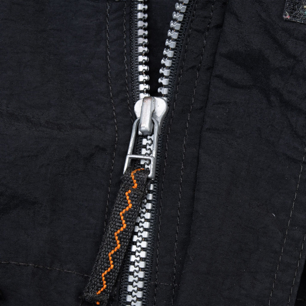 Close-up of silver front zipper with black and orange pull tab
