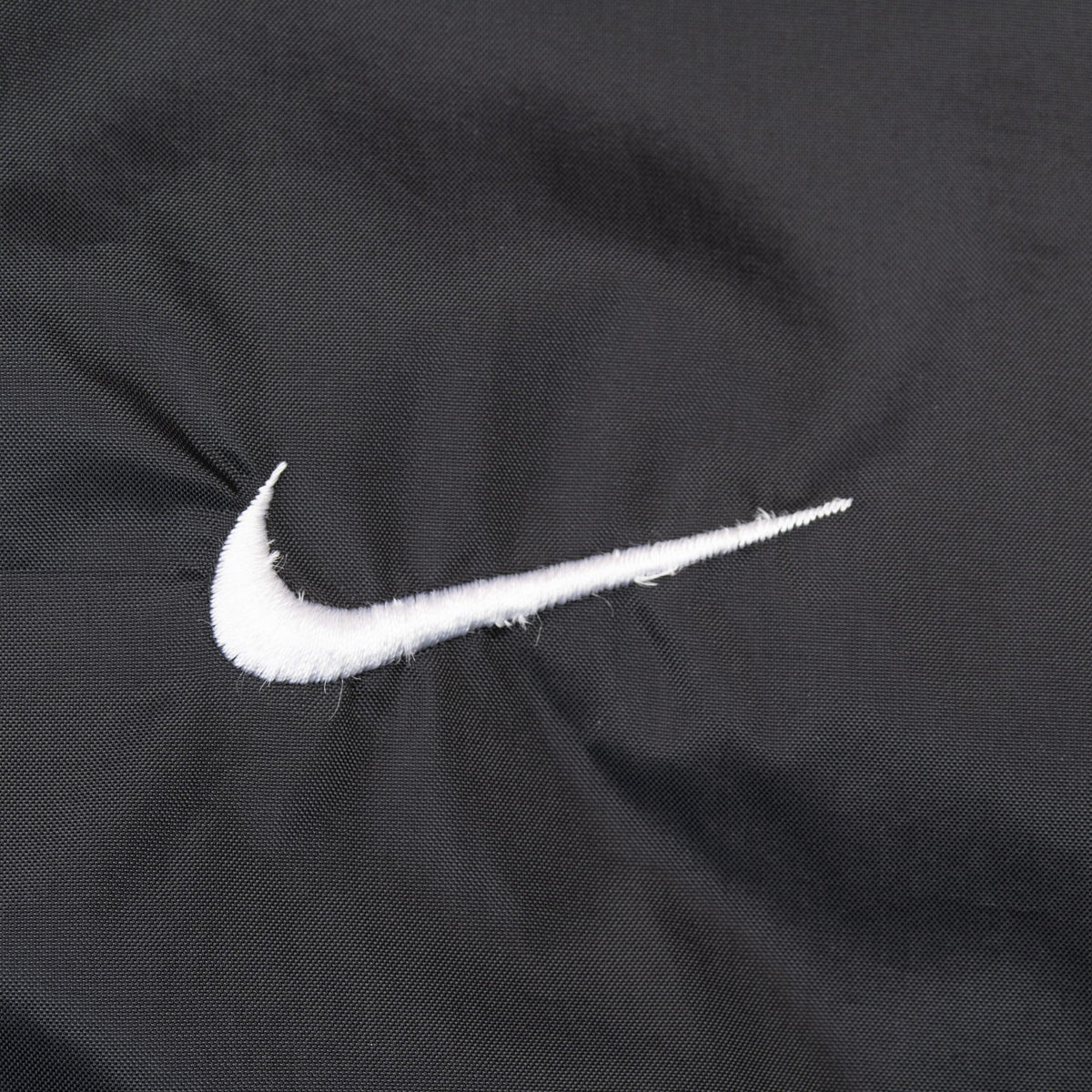 Close-up of white embroidered Nike Swoosh on black jacket fabric