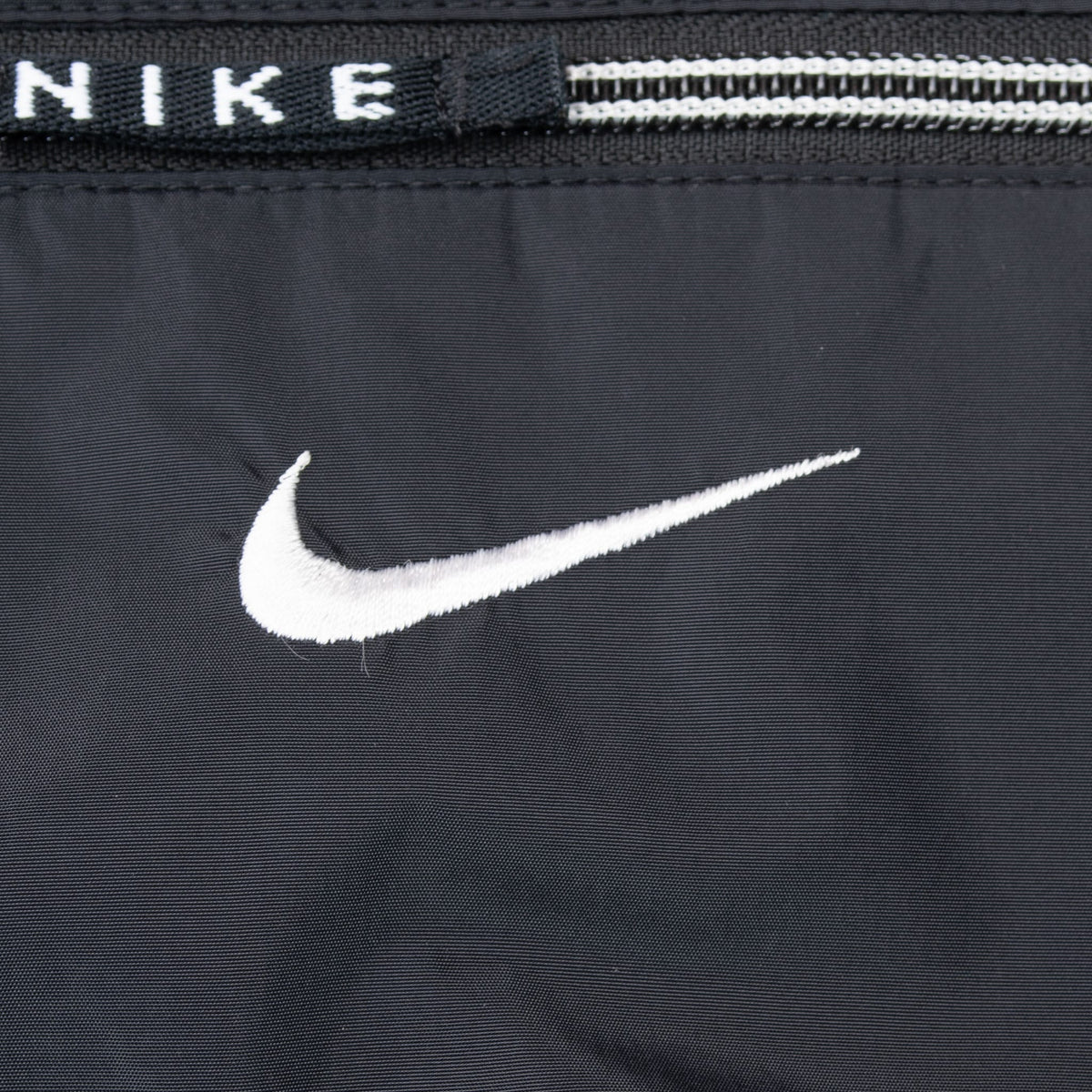 Close-up of white embroidered Nike Swoosh below zippered chest pocket
