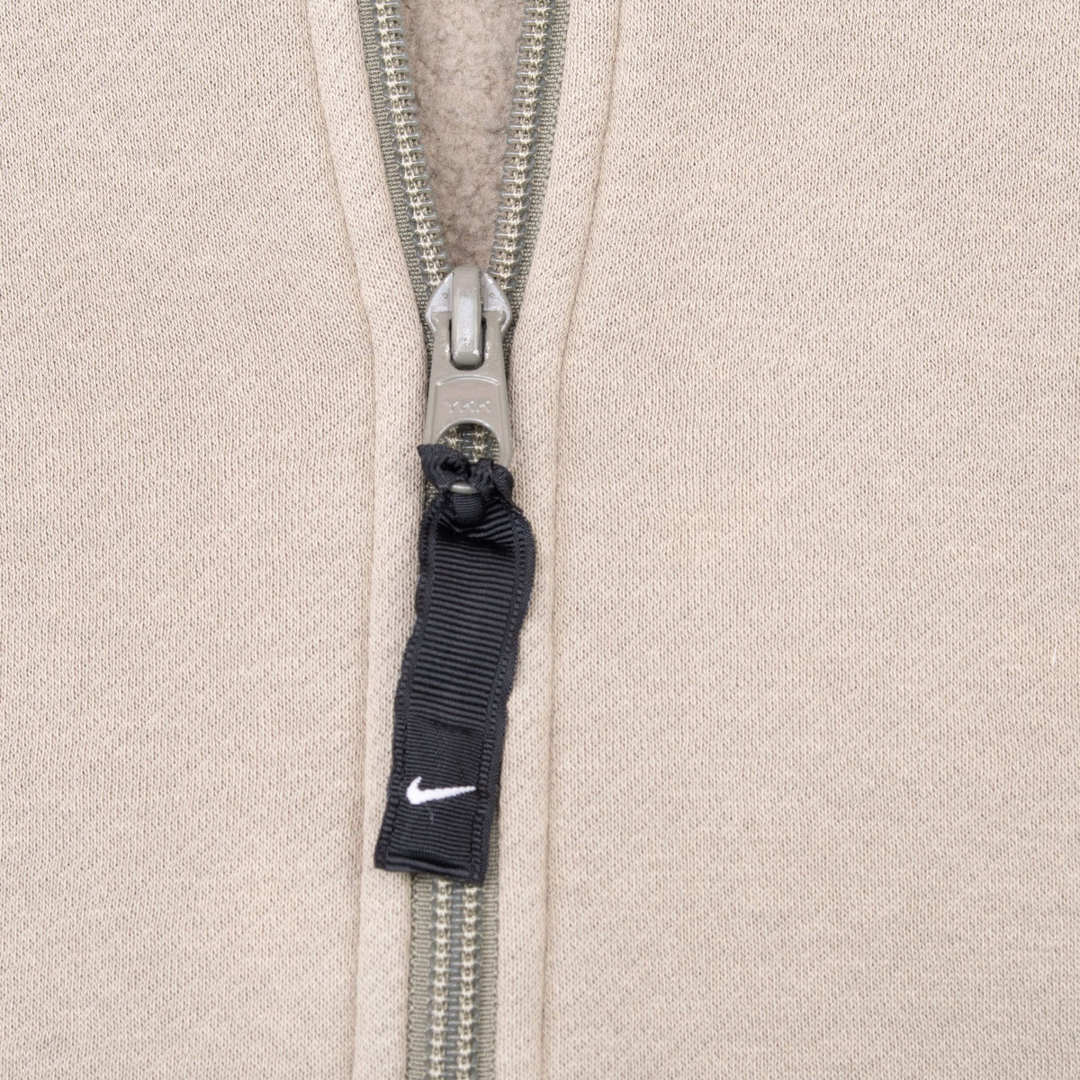 Close-up of metal quarter-zip closure with black Nike Swoosh fabric pull tab