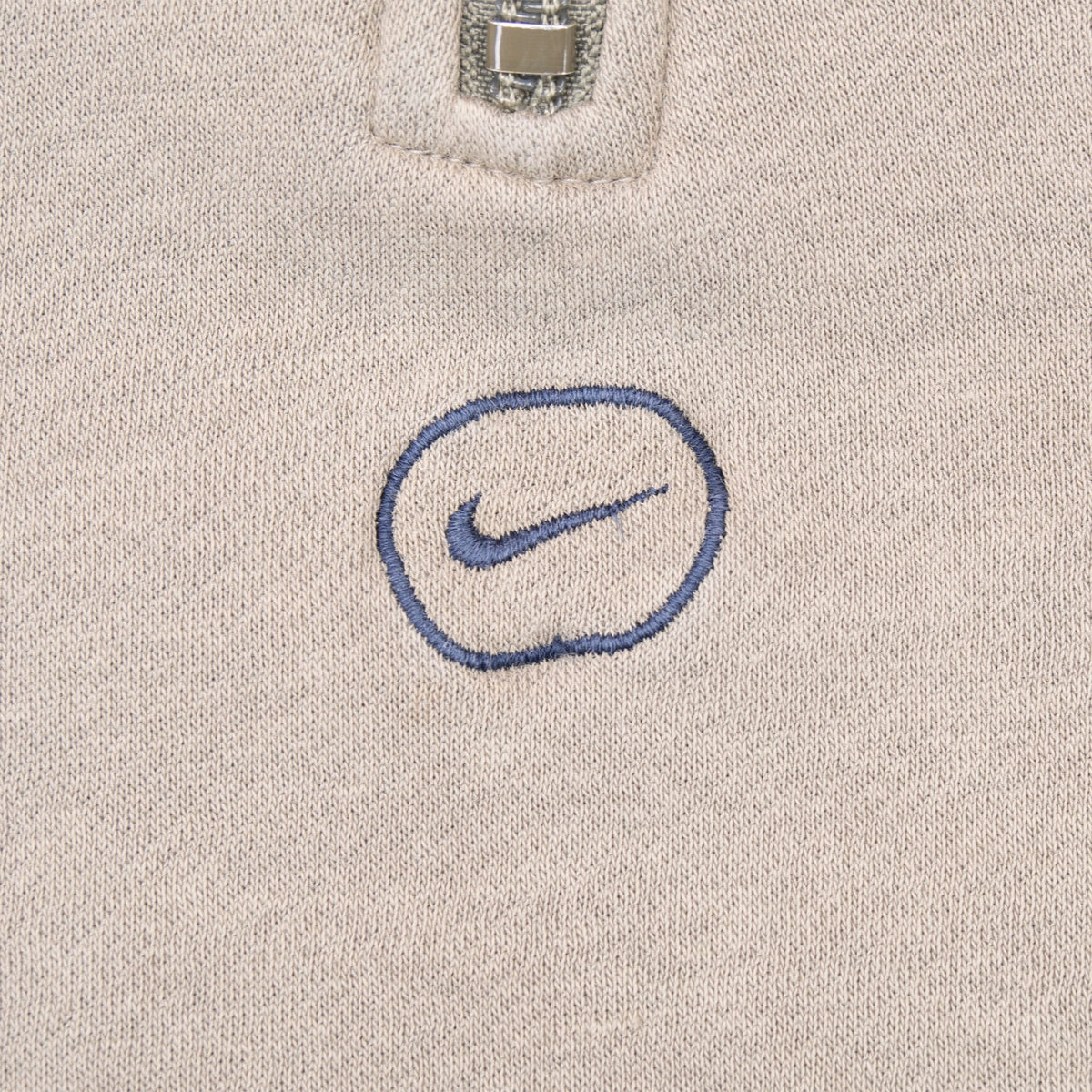 Close-up of navy Swoosh emblem embroidered below the quarter-zip