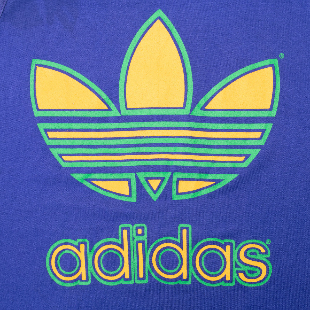 Close-up of yellow and green Adidas Trefoil spellout print on purple fabric