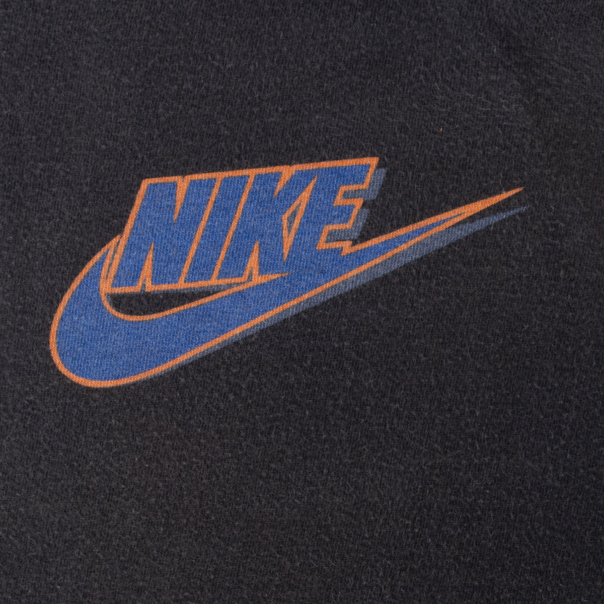 Close-up of blue Nike Swoosh chest print with orange outline on black fabric