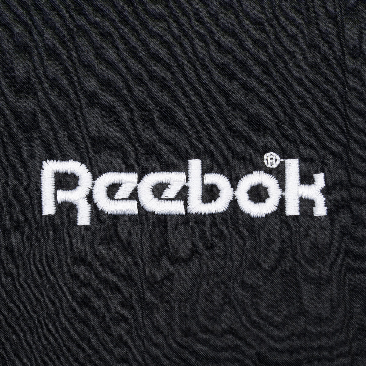 Close-up of white embroidered Reebok chest logo on black fabric