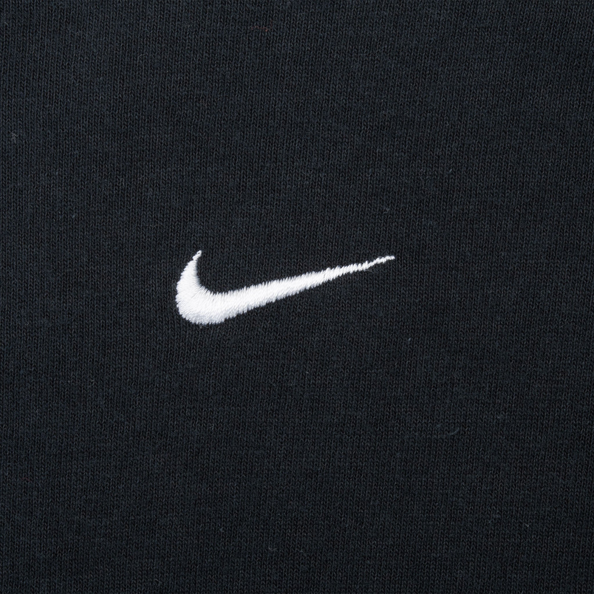 Close-up of white embroidered Nike Swoosh on black chest fabric