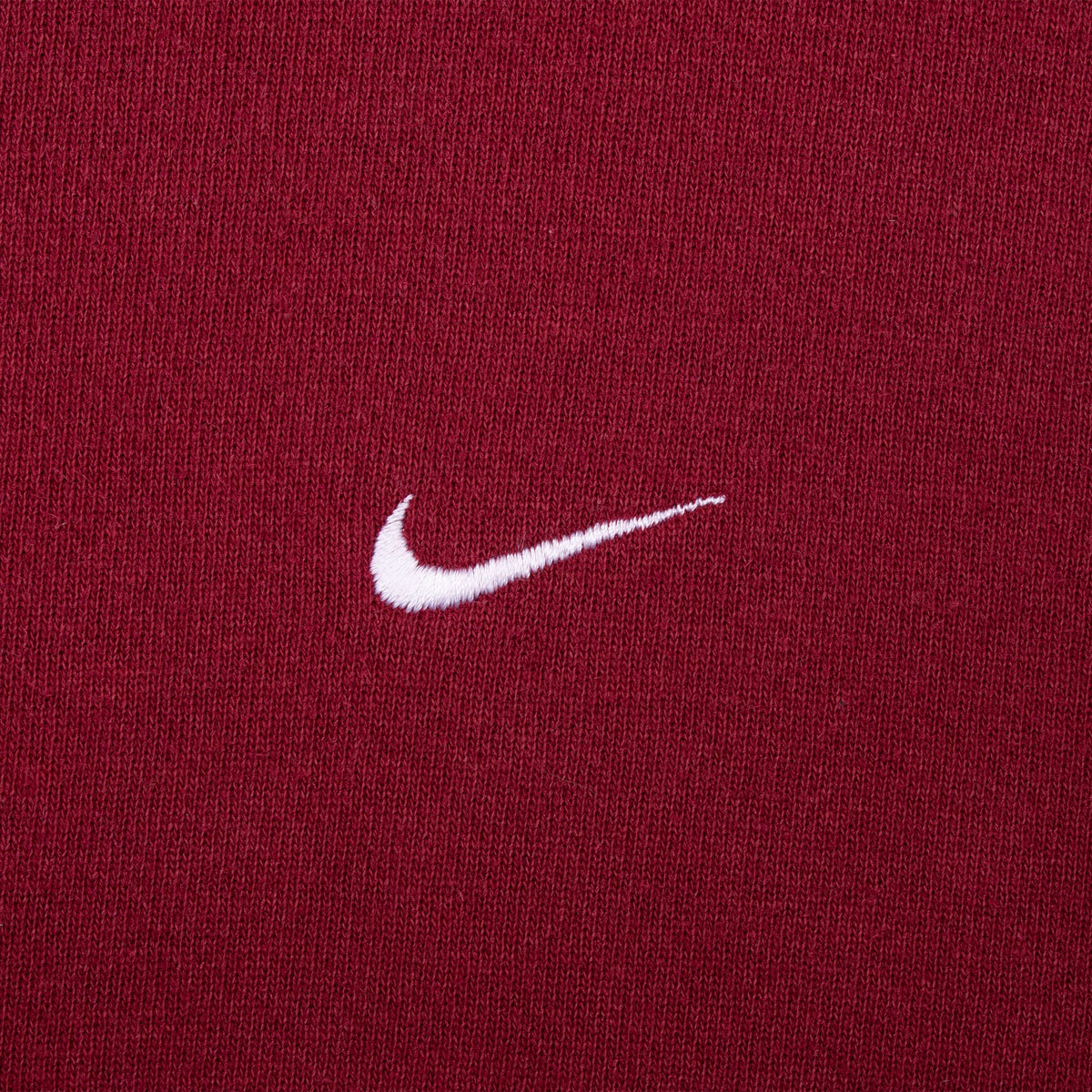 Close-up of white embroidered Nike Swoosh on burgundy fabric