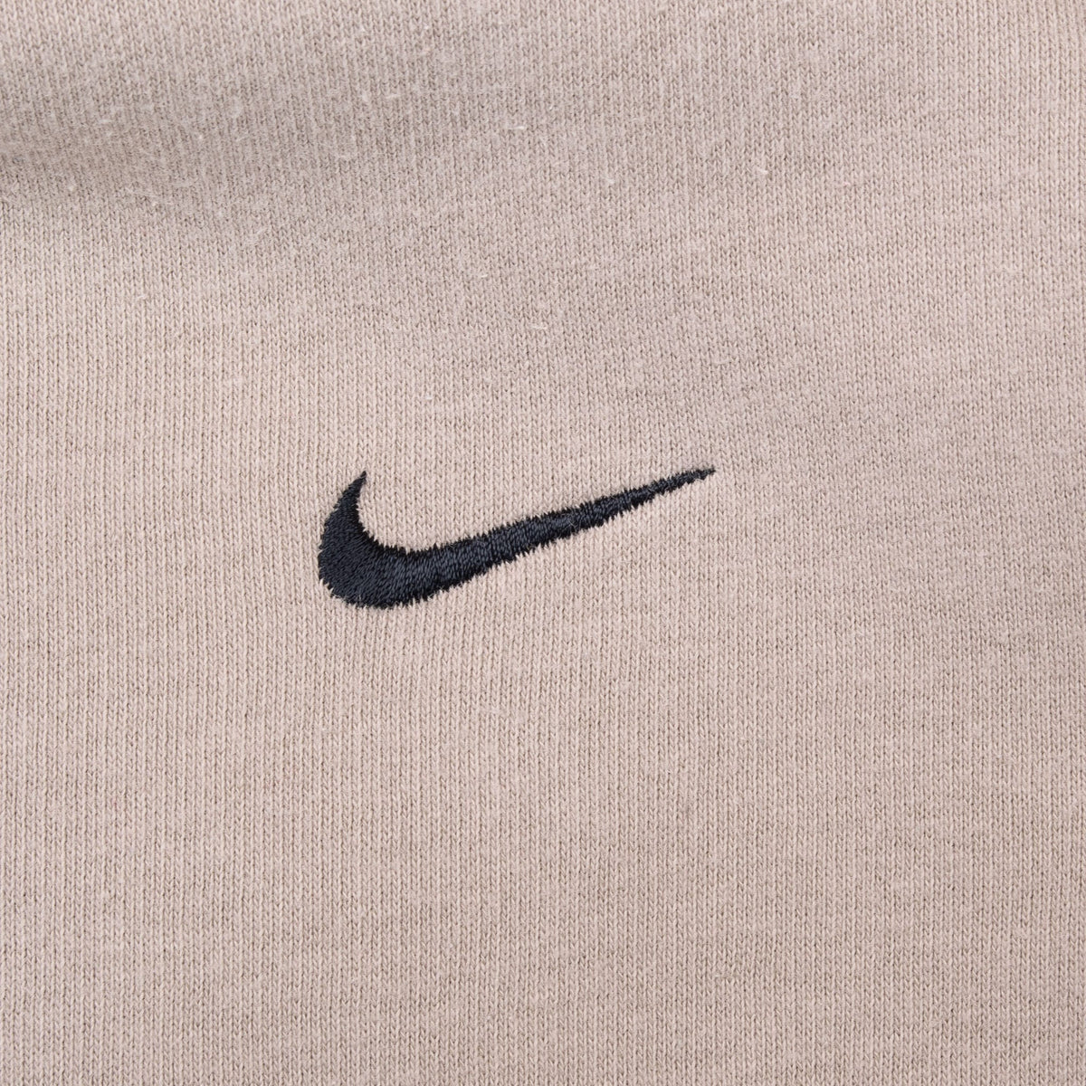 Close-up of black Nike Swoosh embroidery on beige sweatshirt chest
