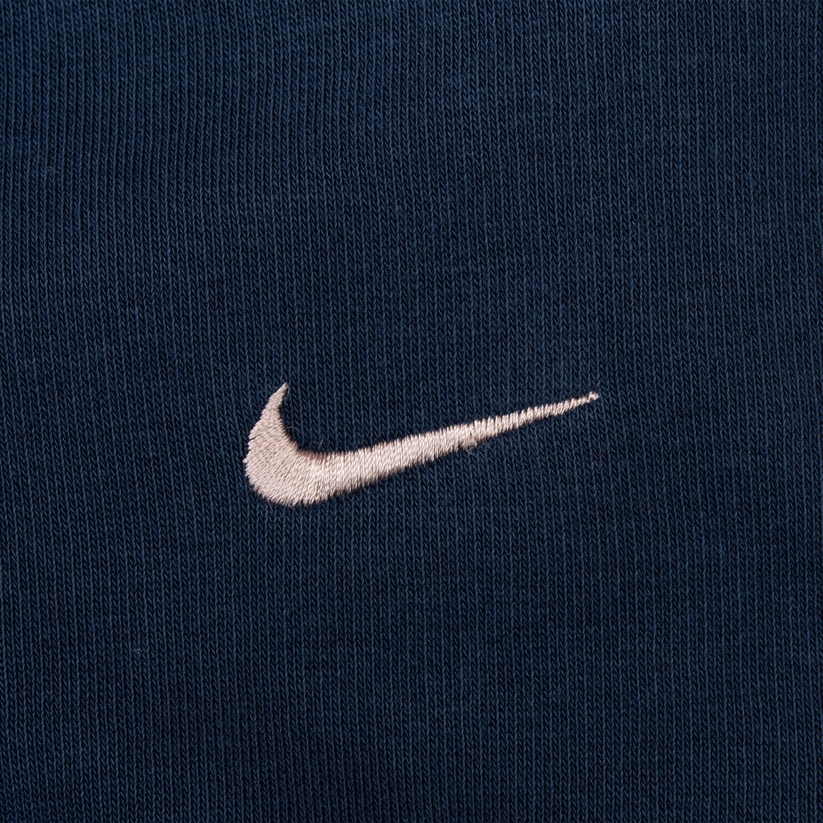 Close-up of contrasting embroidered Nike Swoosh on navy blue fabric