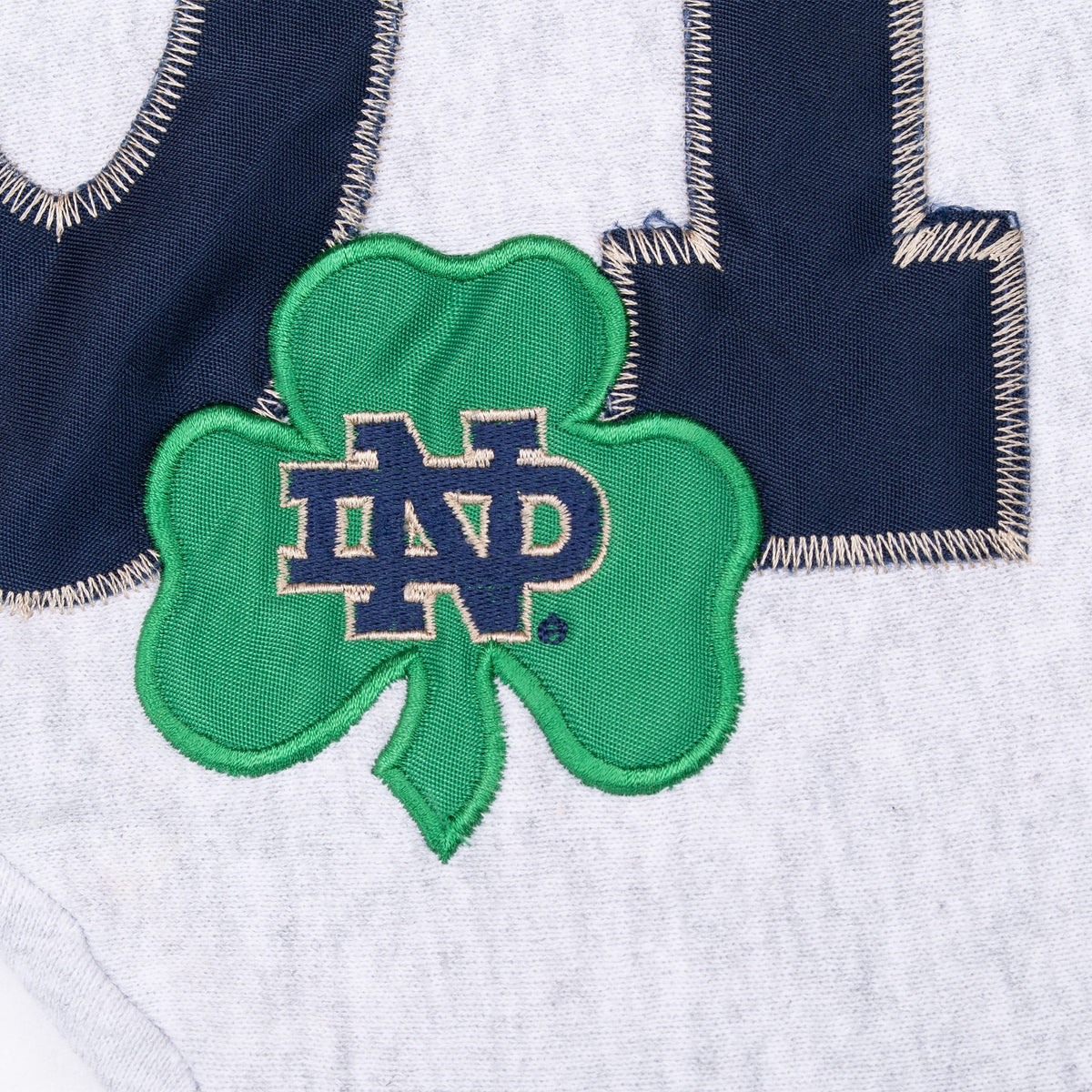 Close-up of green shamrock appliqué with interlocking ND logo over navy lettering