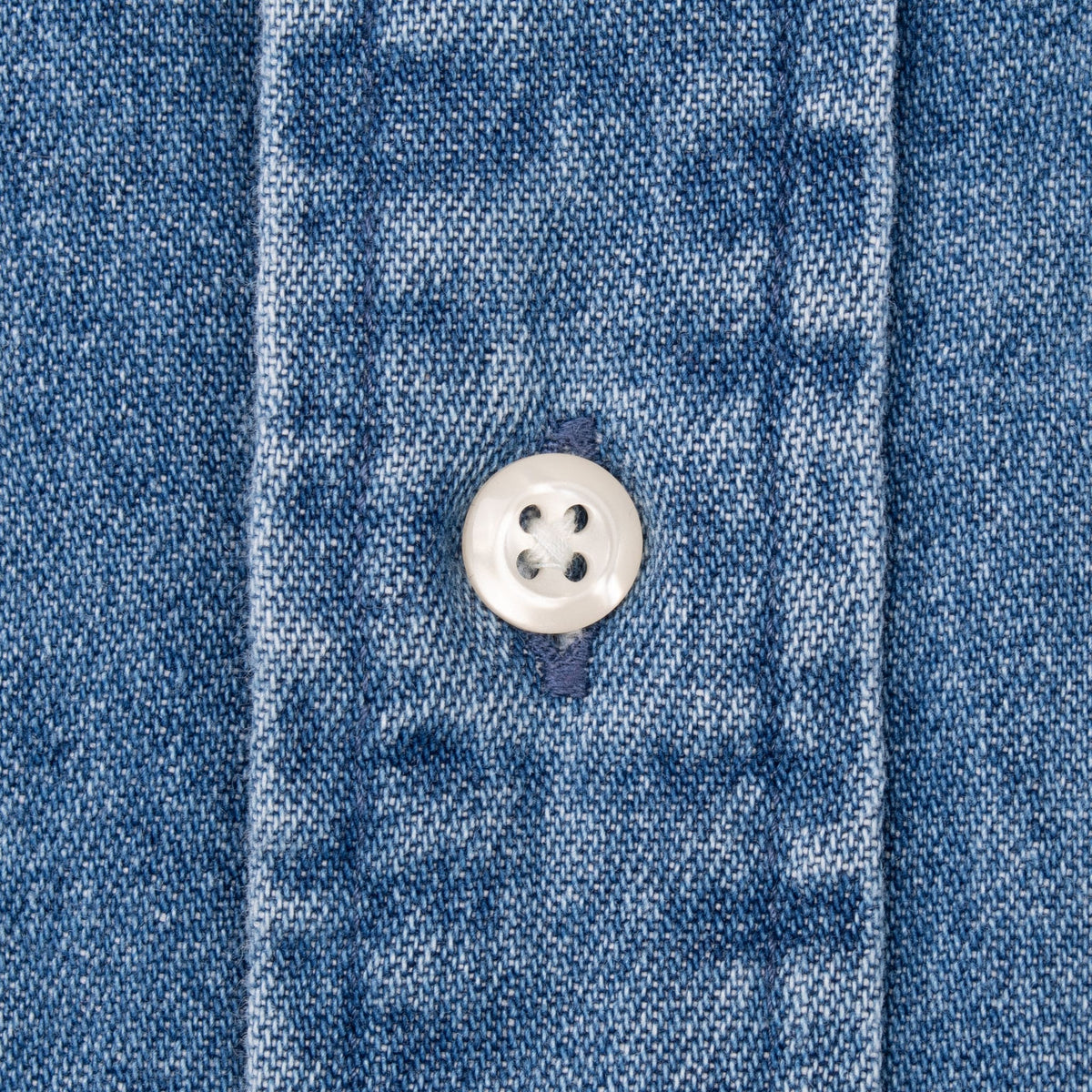 Close-up of white four-hole button and stitching on blue denim shirt