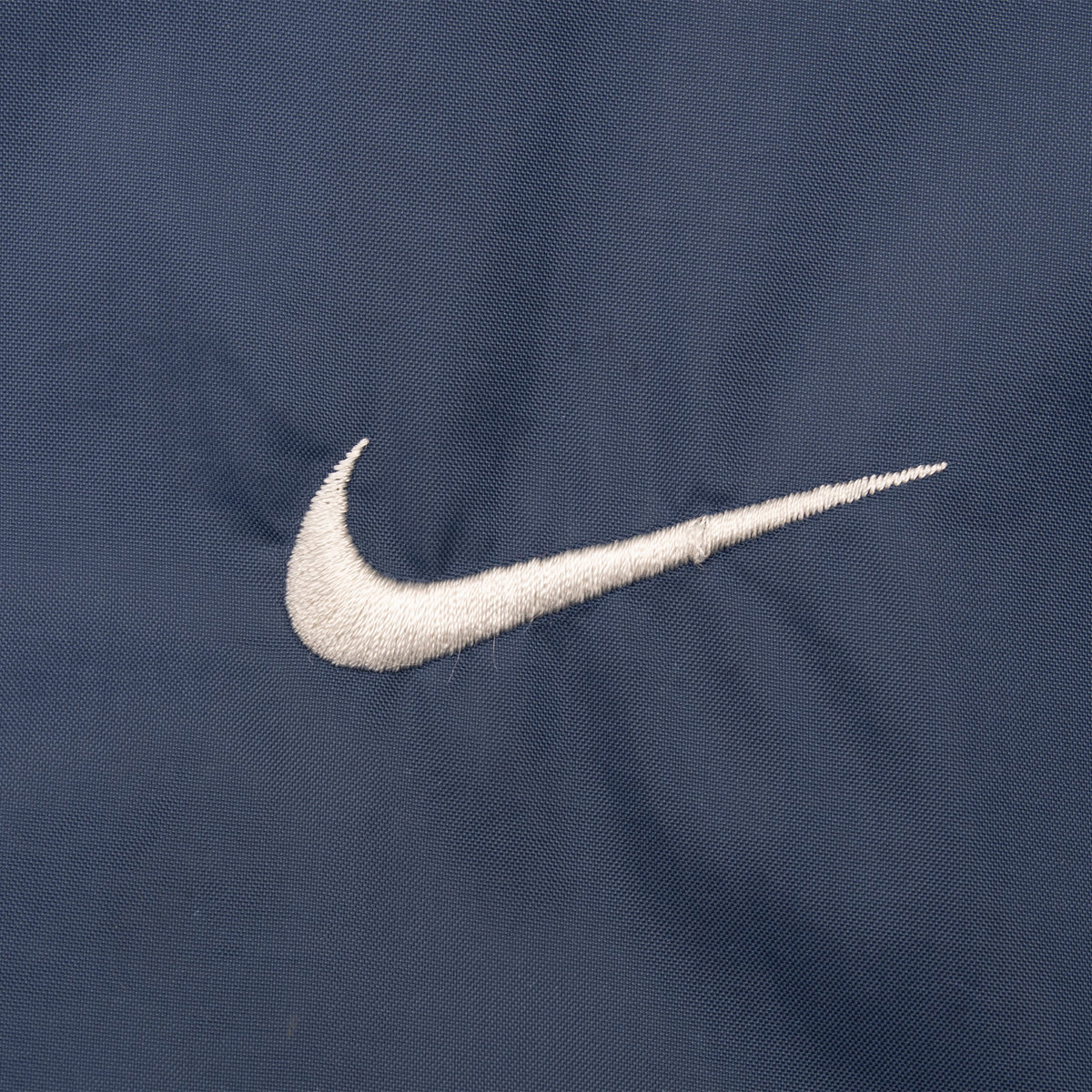 Close-up of white Nike Swoosh embroidery on navy blue fabric