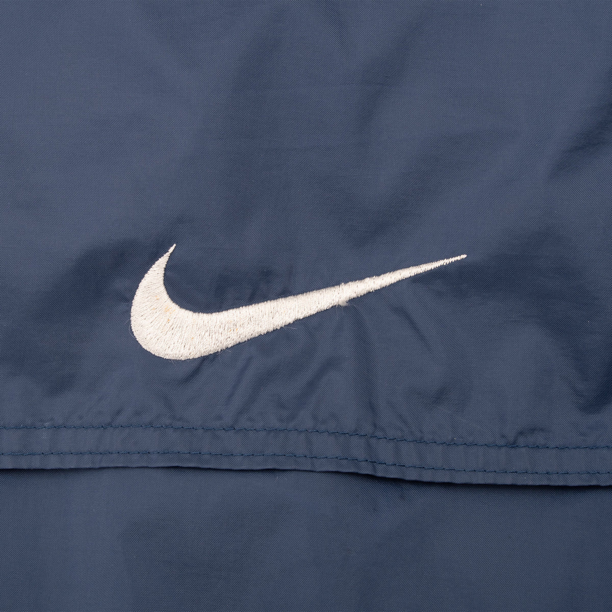 Close-up of white Nike Swoosh embroidery above the back vent seam