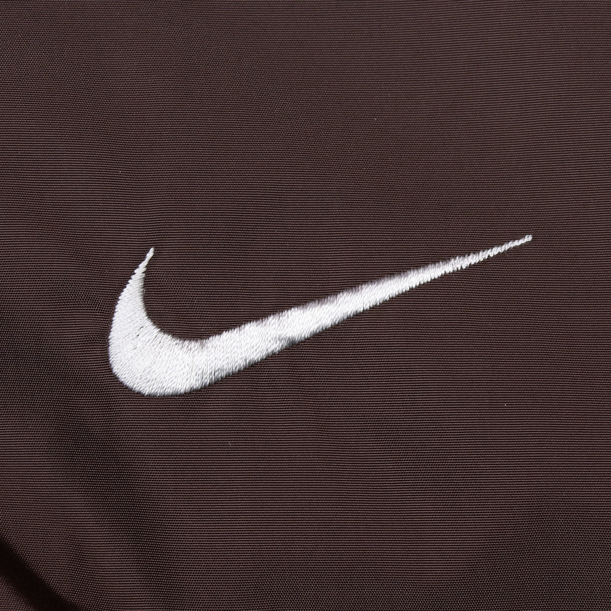 Close-up of white embroidered Nike Swoosh on brown fabric