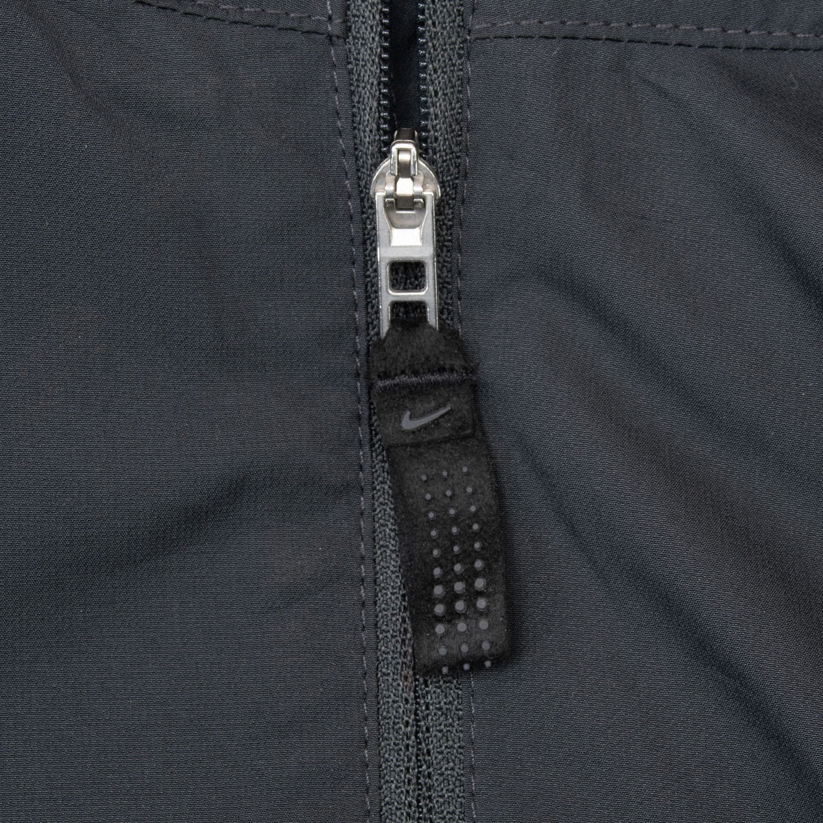Close-up of black Nike Golf windbreaker zipper pull with small Swoosh