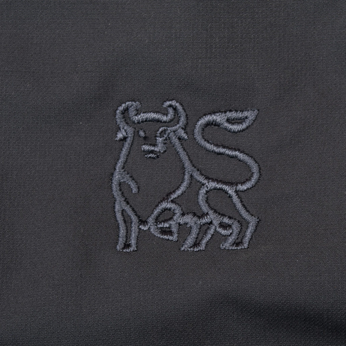 Close-up of tonal bull embroidery on upper back of black Nike Golf windbreaker