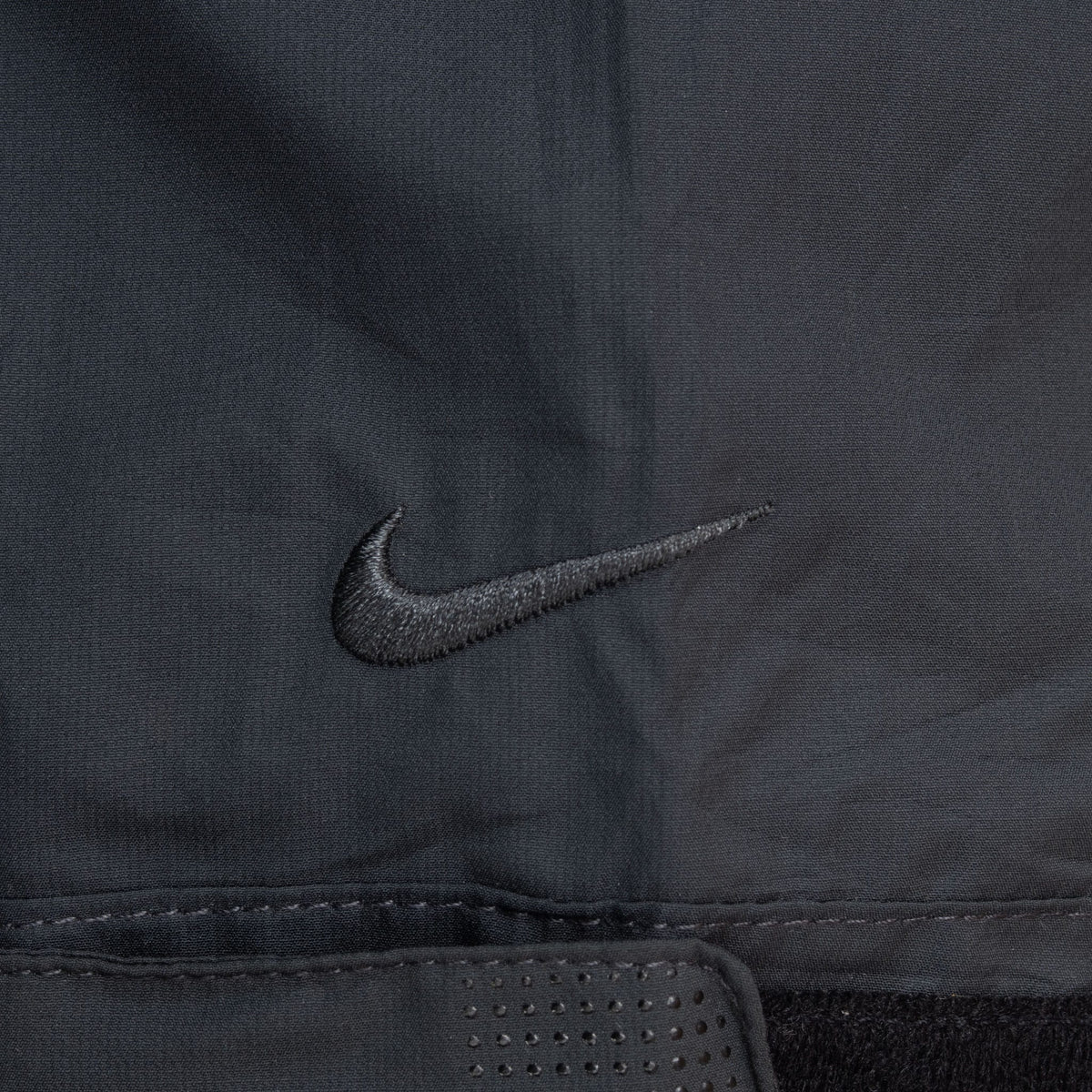Close-up of tonal Nike Swoosh embroidery near cuff tab on black windbreaker