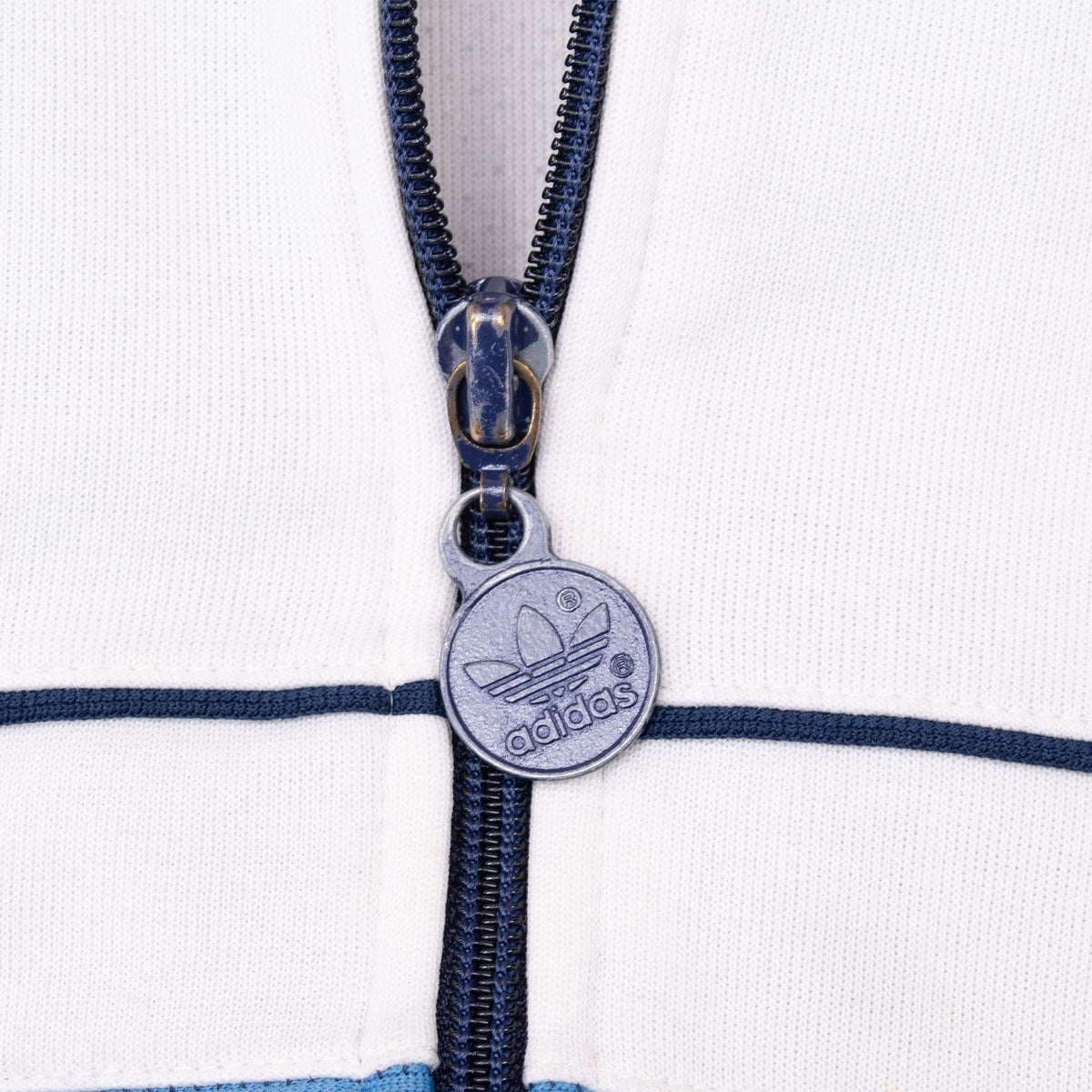 Close-up of round Adidas Trefoil zipper pull on navy zipper