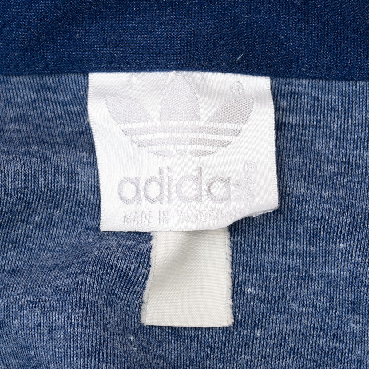 Close-up of white adidas Trefoil neck label inside navy track jacket