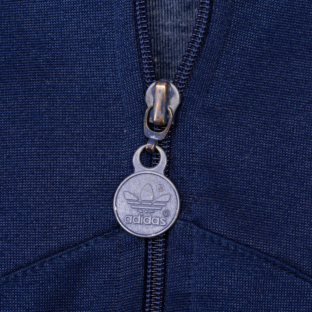 Close-up of metal adidas Trefoil zipper pull on navy track jacket