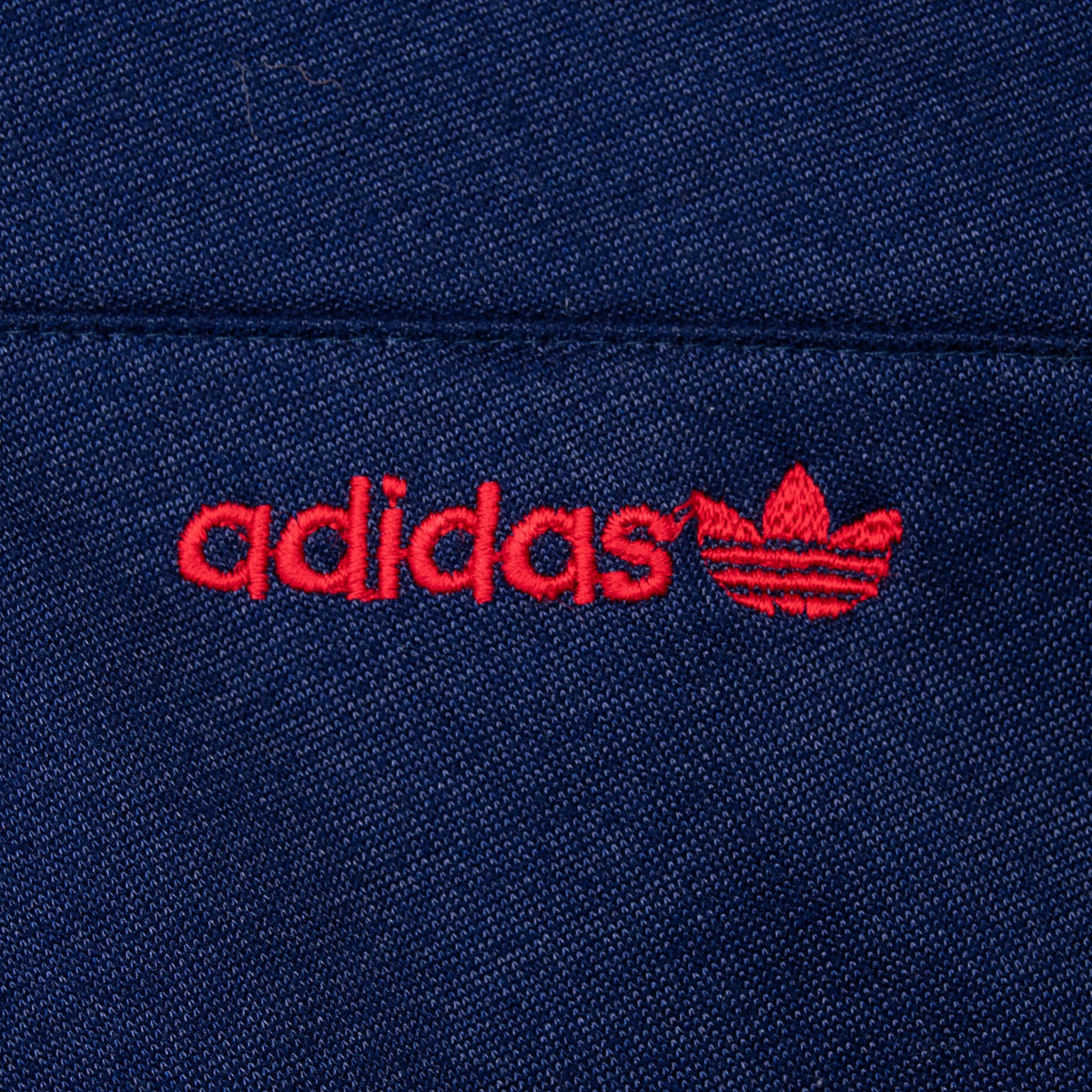Close-up of red adidas Trefoil embroidery on navy track jacket chest