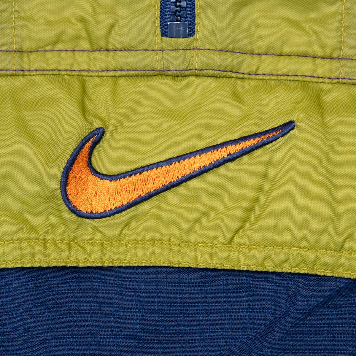 Close-up of orange and navy embroidered Nike Swoosh on green front panel