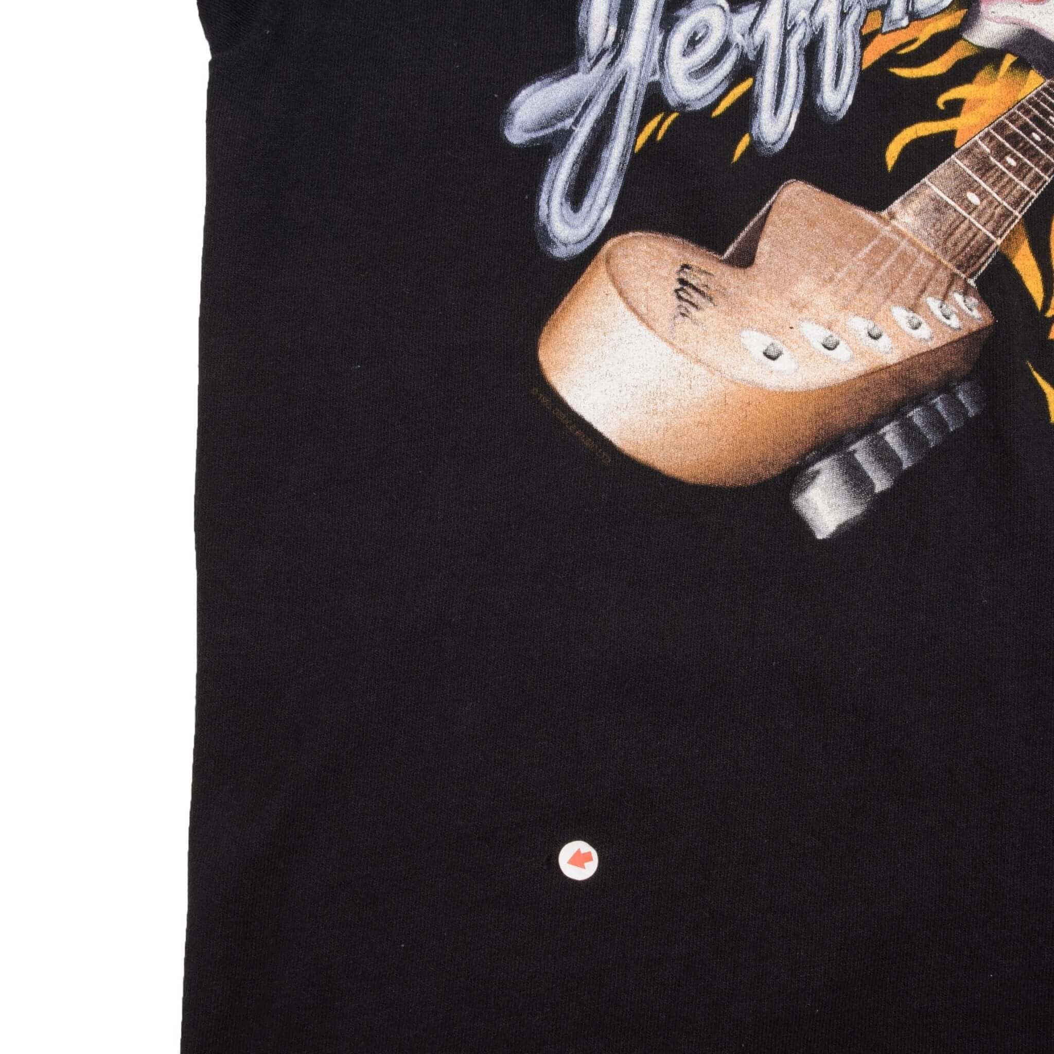 Lower front detail of black T-shirt with a small spot marked below the guitar graphic