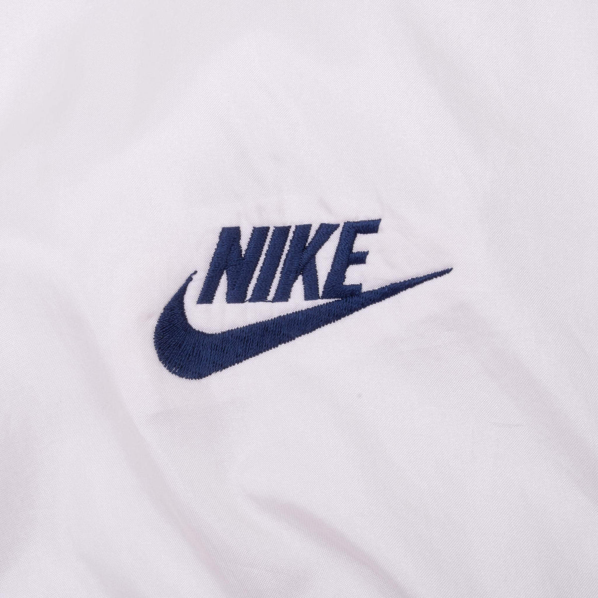 Close-up of navy Nike logo embroidered on white jacket fabric