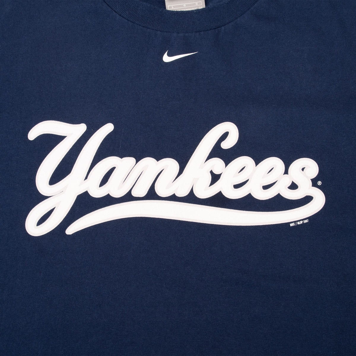 Close-up of white Yankees script and Nike Swoosh on navy T-shirt
