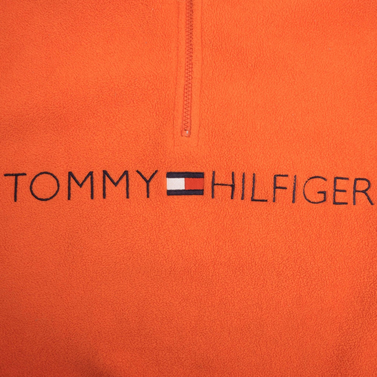 Close-up of embroidered Tommy Hilfiger chest logo and quarter zip on orange fleece