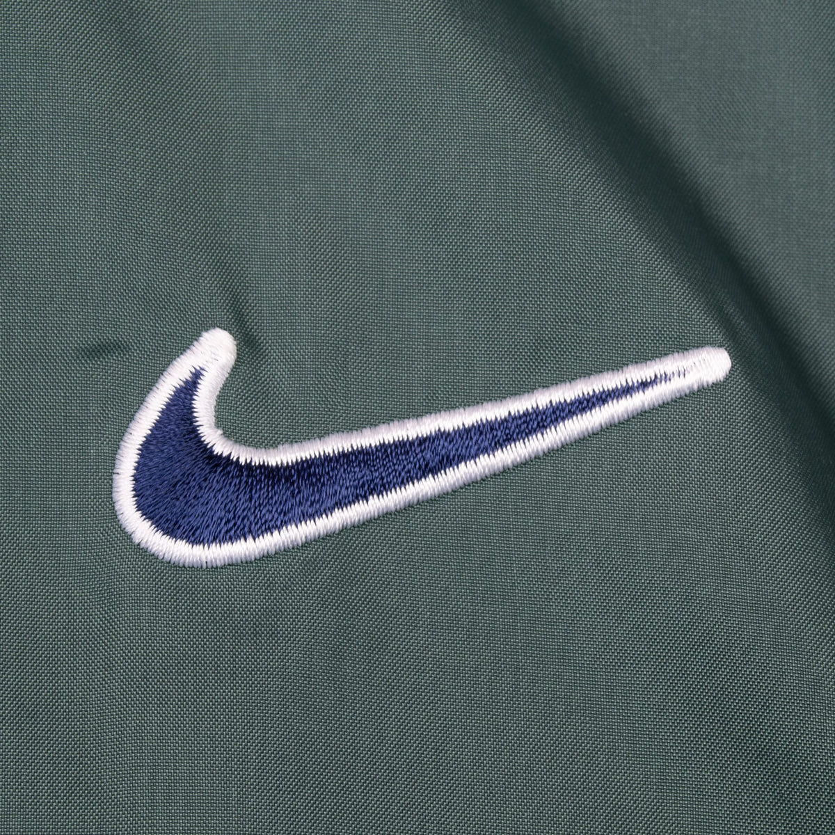 Close-up of navy and white embroidered Nike Swoosh on green chest