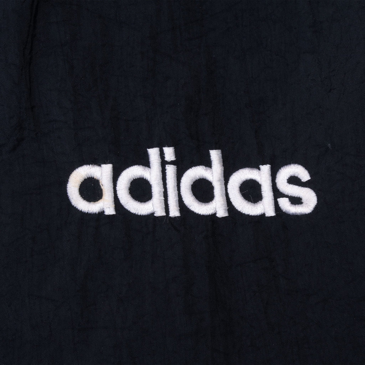 Close-up of white Adidas embroidery on black jacket chest