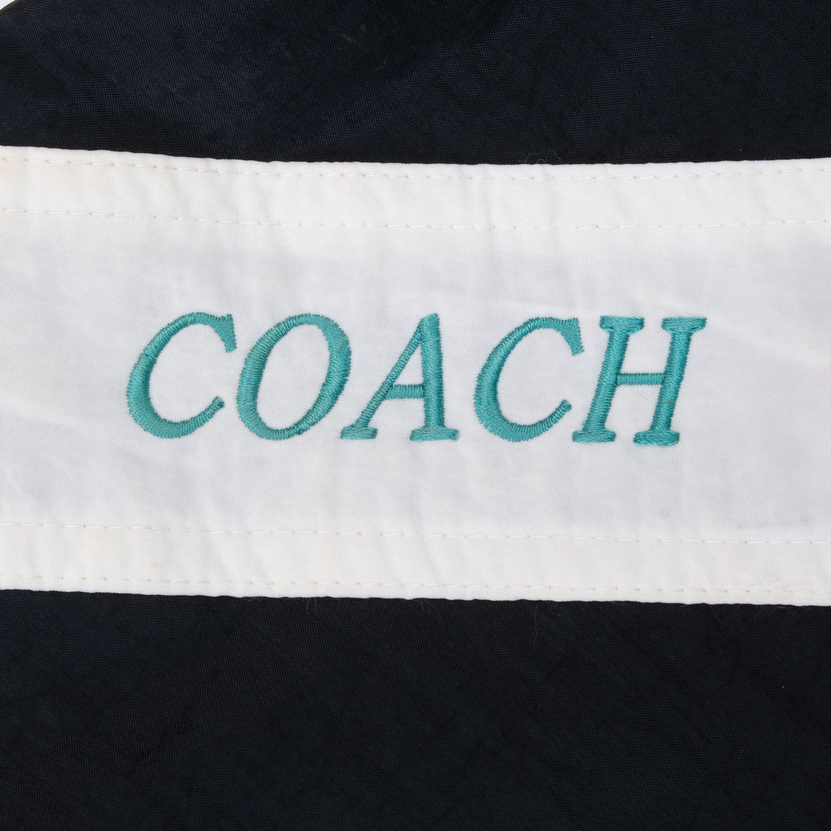 Close-up of teal COACH embroidery on white shoulder stripe
