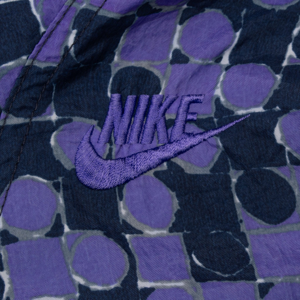 Close-up of purple embroidered Nike Swoosh logo on dotted jacket chest