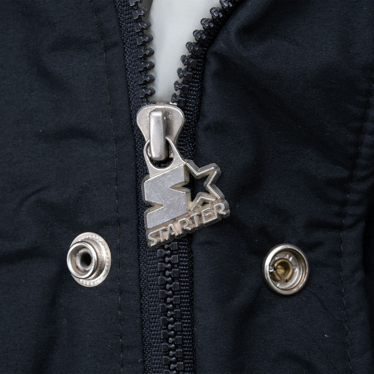 Close-up of metal Starter logo zipper pull and snap fasteners on black jacket