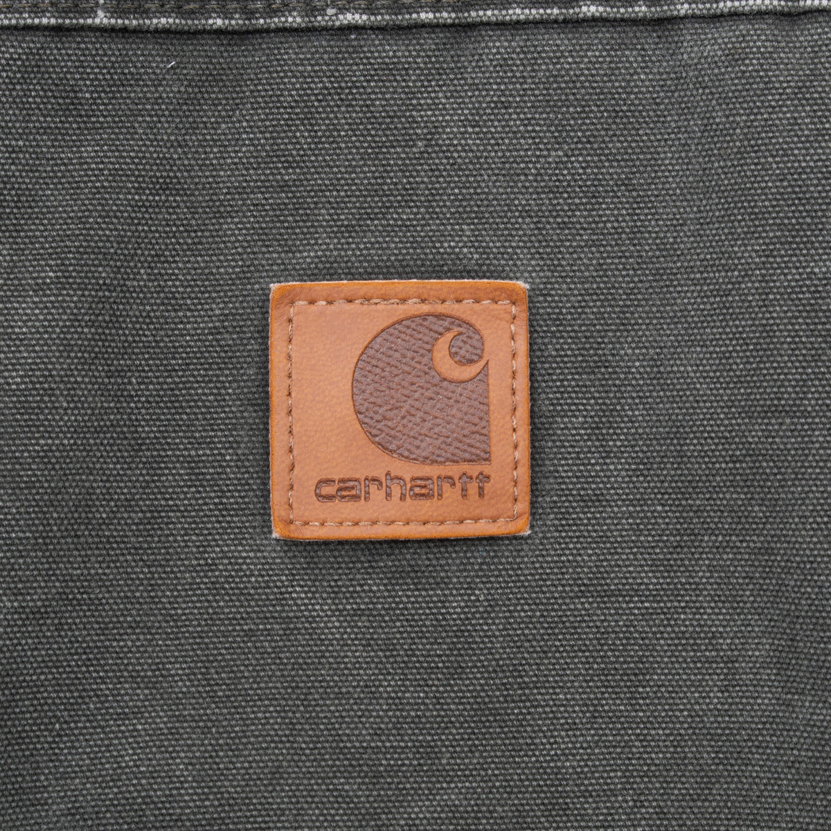 Close-up of brown Carhartt logo patch stitched on dark green vest fabric