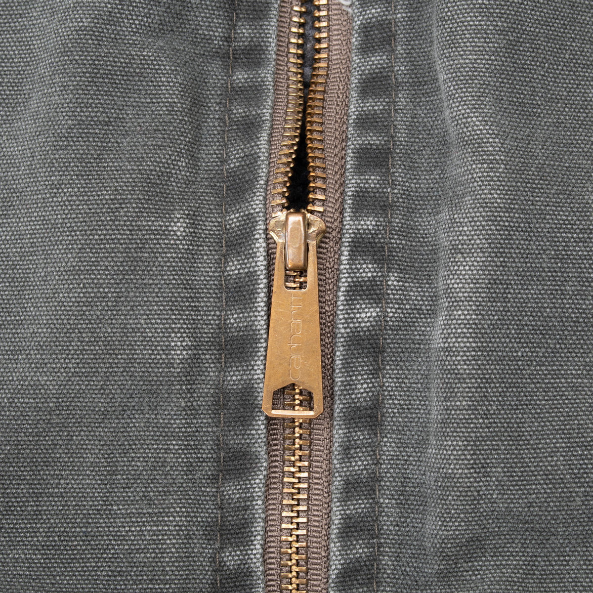 Close-up of brass-tone Carhartt zipper and pull on dark green vest fabric