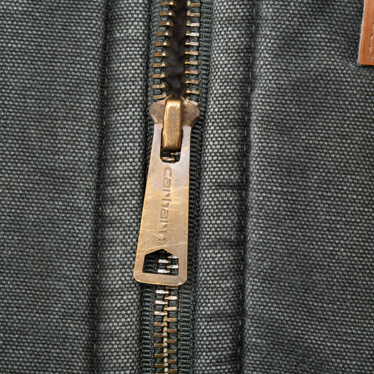 Close-up of brass-tone Carhartt zipper pull on green vest